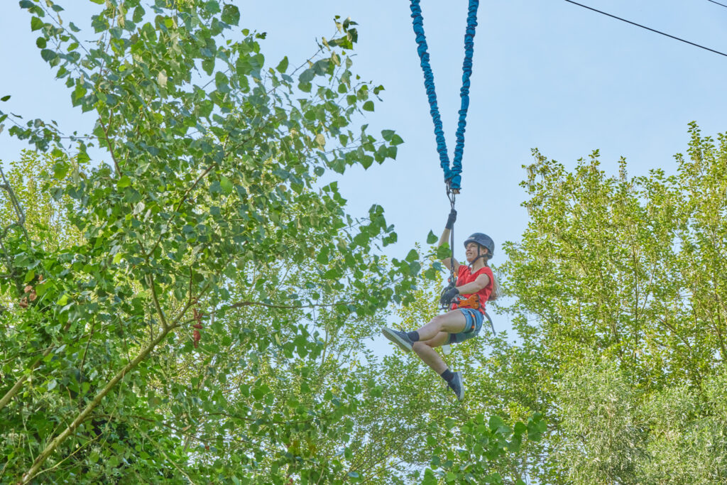 Vrouw zit vast aan de bungeejump tussen de bomen. Ze heeft een uitgestrekt been en arm.