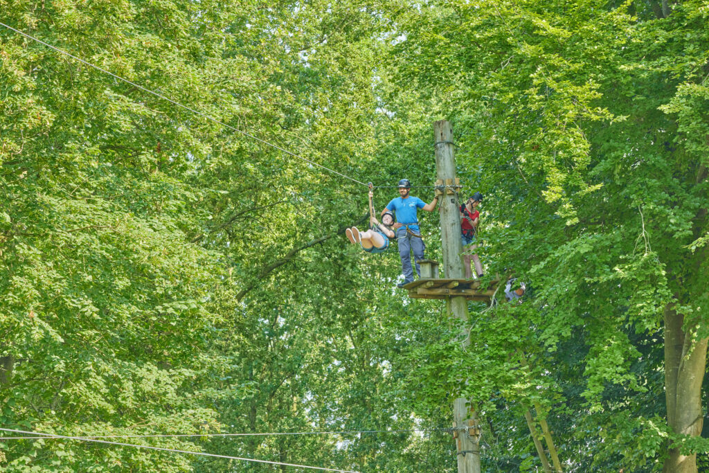 Groep staat op platform te wachten voor de zipline terwijl 1 vrouw al naar de overkant tokkelt.