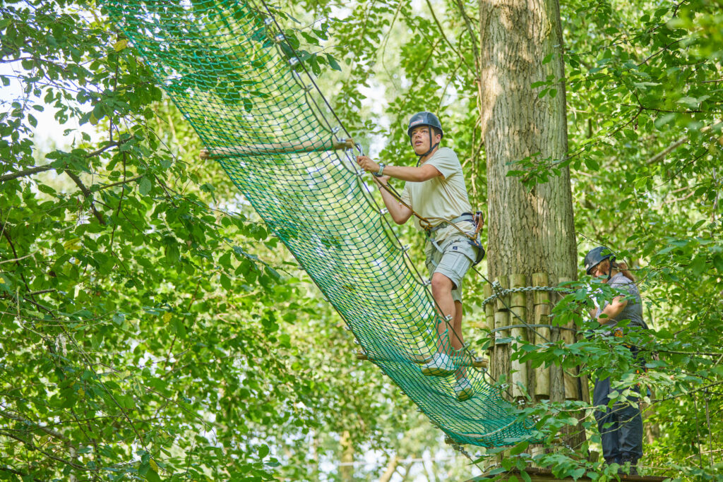 Man klimt over net omhoog tussen de bomen.