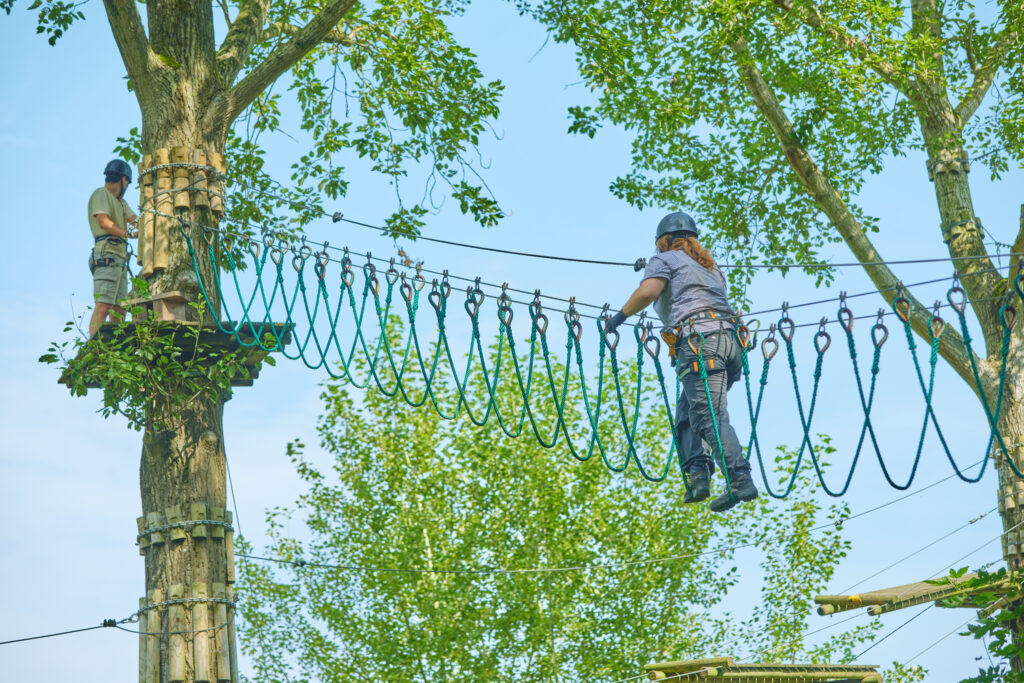 Persoon klimt over een touwbrug naar een hoger gelegen parcours.