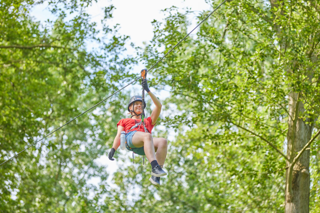 Jongvolwassene vrouw tokkelt naar de overkant. Haar rechterhand hangt ontspannen naast haar lichaam, op haar linkerheup is een waterfles te zien.
