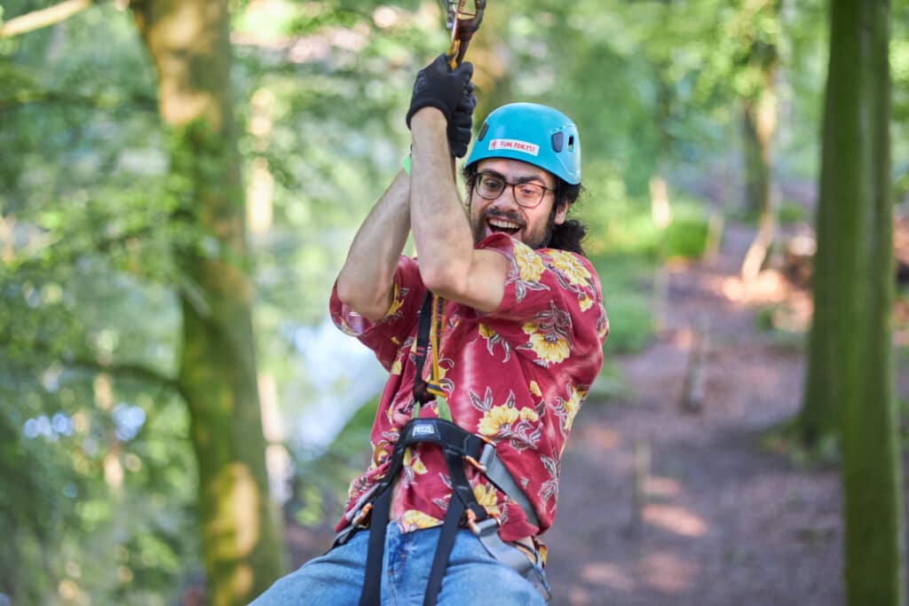 Man wearing a blue helmet and glasses ziplined across with a big smile.