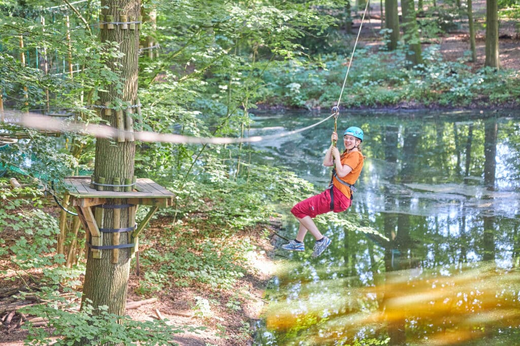 Jongedame met een rode broek ziplined over het water naar de overkant.