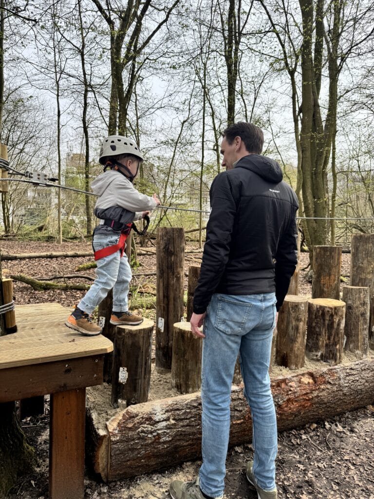 Vader kijkt toe hoe zijn zoontje over verschillende hoogtes boomstammen heen klimt.
