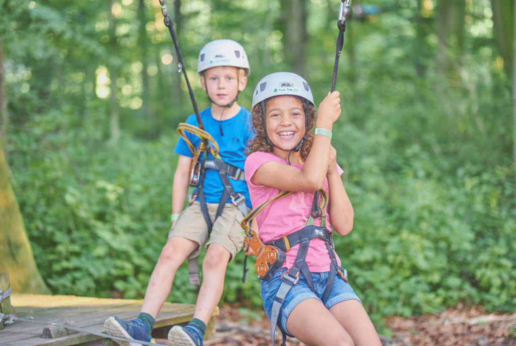 Twee kinderen met een witte helm hangen in het parcours en lachen naar de camera.